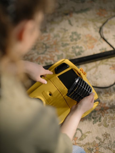 A person holding a yellow portable carpet cleaning machine with a black vent and control panel is performing surface cleaning on an ornate, multicolored area rug with floral patterns. The rug is situa